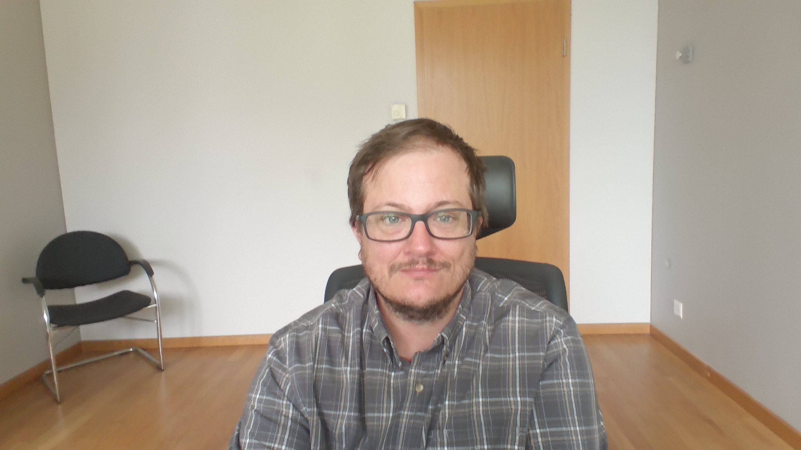 White man with glasses, short brown hair, and a short beard sitting in a computer chair
