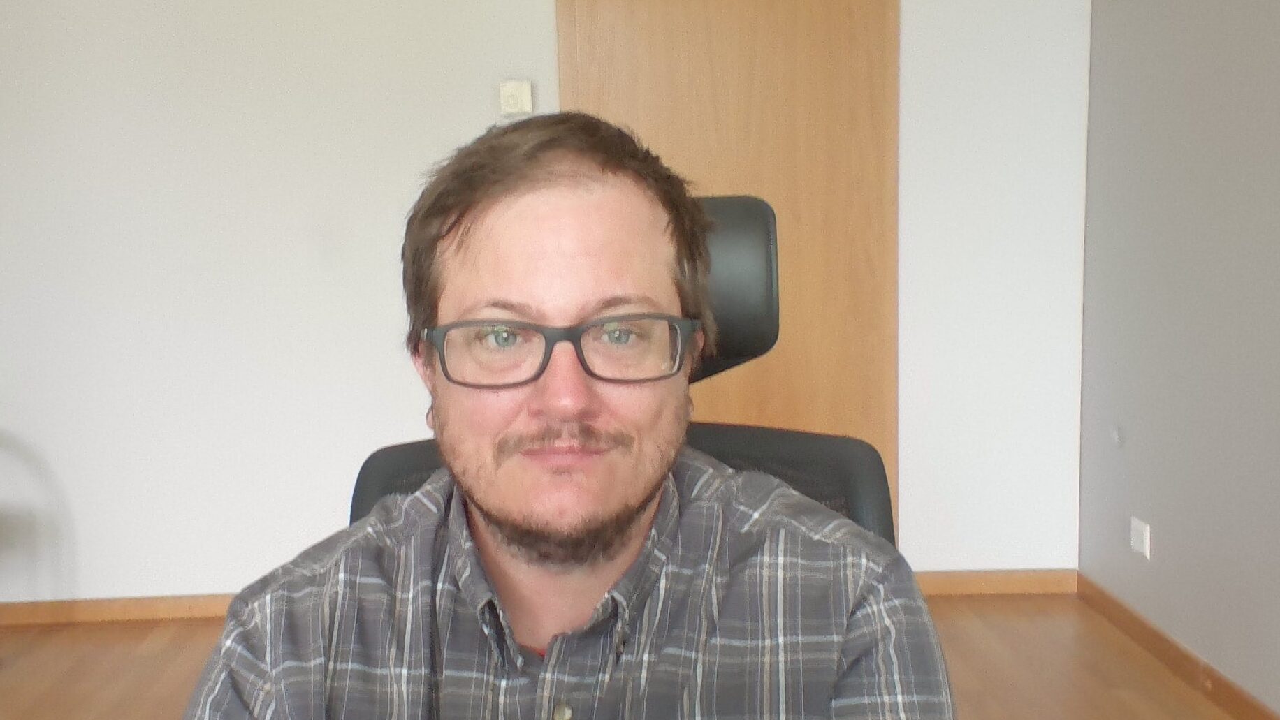 White man with glasses, short brown hair, and a short beard sitting in a computer chair